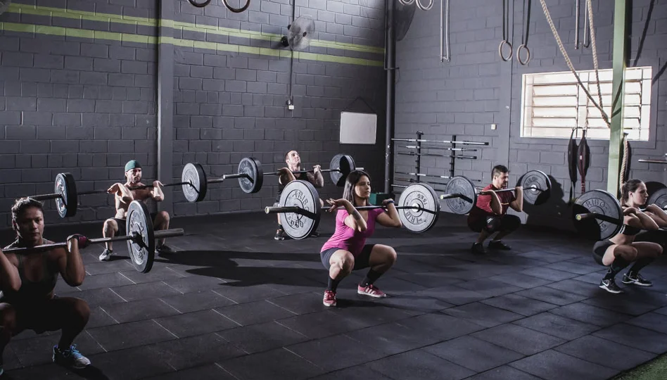Aula de Crossfit com os alunos fazendo agachamento com peso